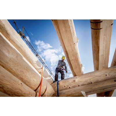 Workers on a building site are installing large wooden beams. A crane and blue sky can be seen in the background.