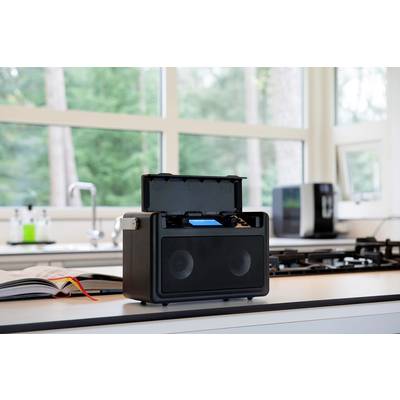 Portable speaker on a worktop in a modern kitchen; window with a view of greenery in the background.