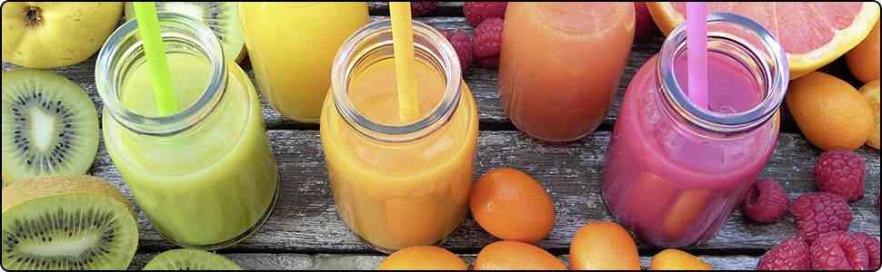 Four colourful fruit smoothies in glasses with straws sit on a wooden table, surrounded by kiwi, orange, and raspberry fruits.