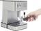 'A person is holding a portafilter next to a silver espresso machine.'