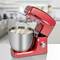 Red stand mixer with mixing bowl full of dough, set up in a modern kitchen. Two blurred people in the background.