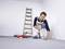 A man in workwear is laying floor tiles in a room. A ladder stands in the background, with tools lying nearby.