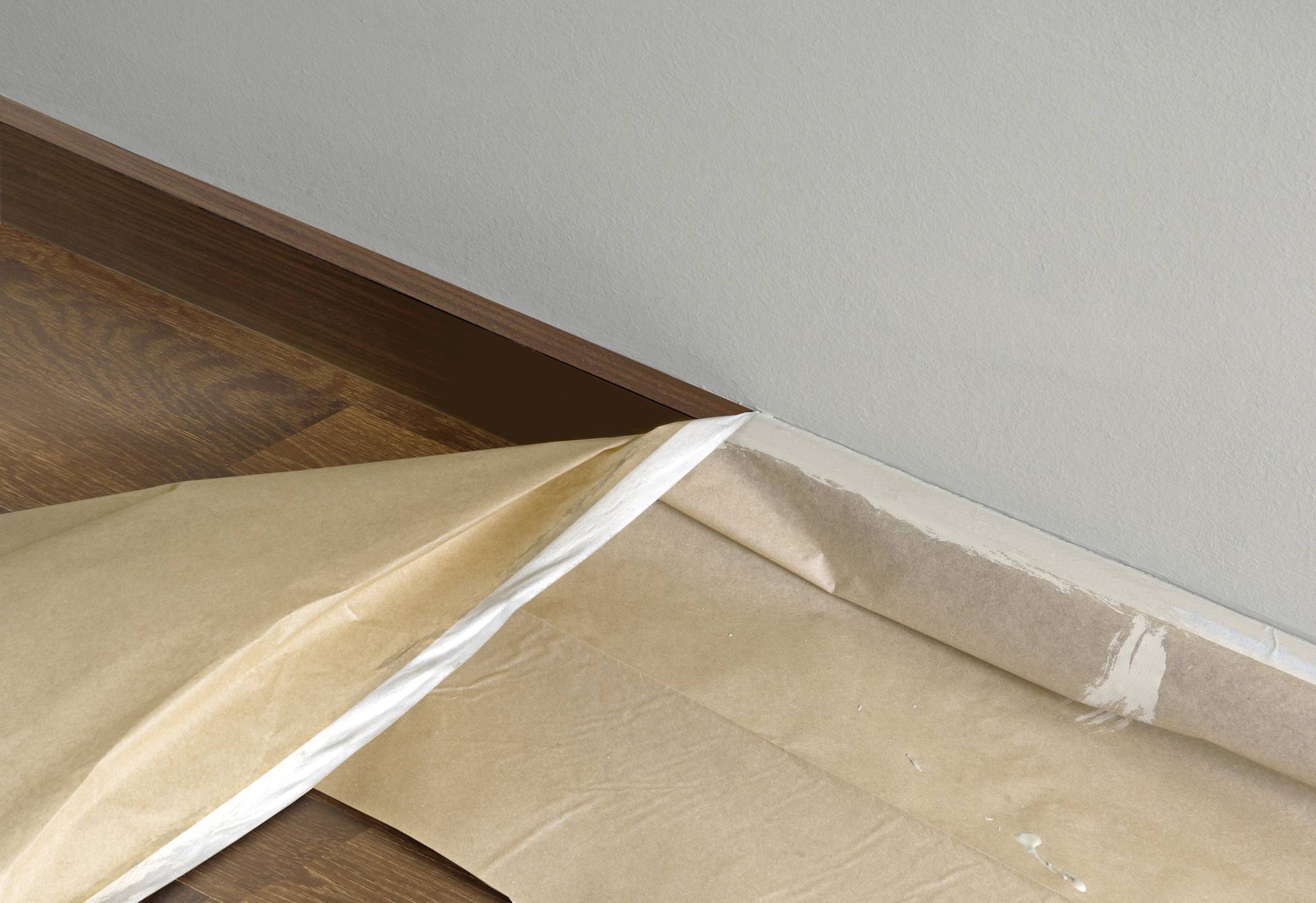 A room with a wooden floor, with brown protective paper taped along the edge next to the wall to protect the floor.