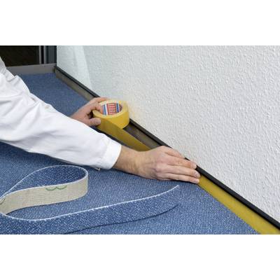 A person is sticking yellow masking tape along the edge of a carpet next to a white wall to create a clean finish.