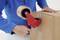 A person is sealing a cardboard box with tape using a red and blue handheld tape dispenser.