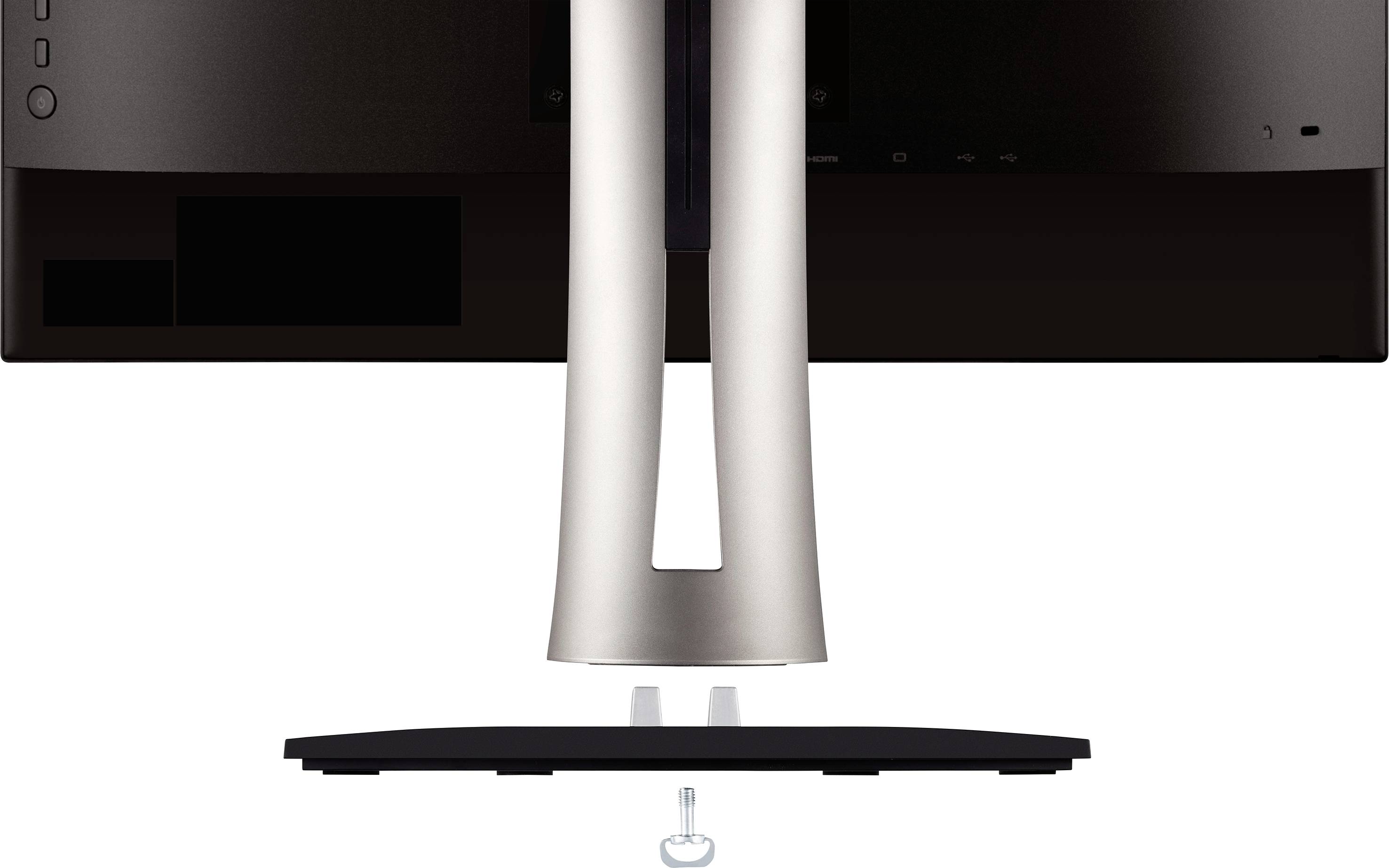 A computer monitor is shown from behind, mounted on a stand. A screw lies underneath to ensure stability.