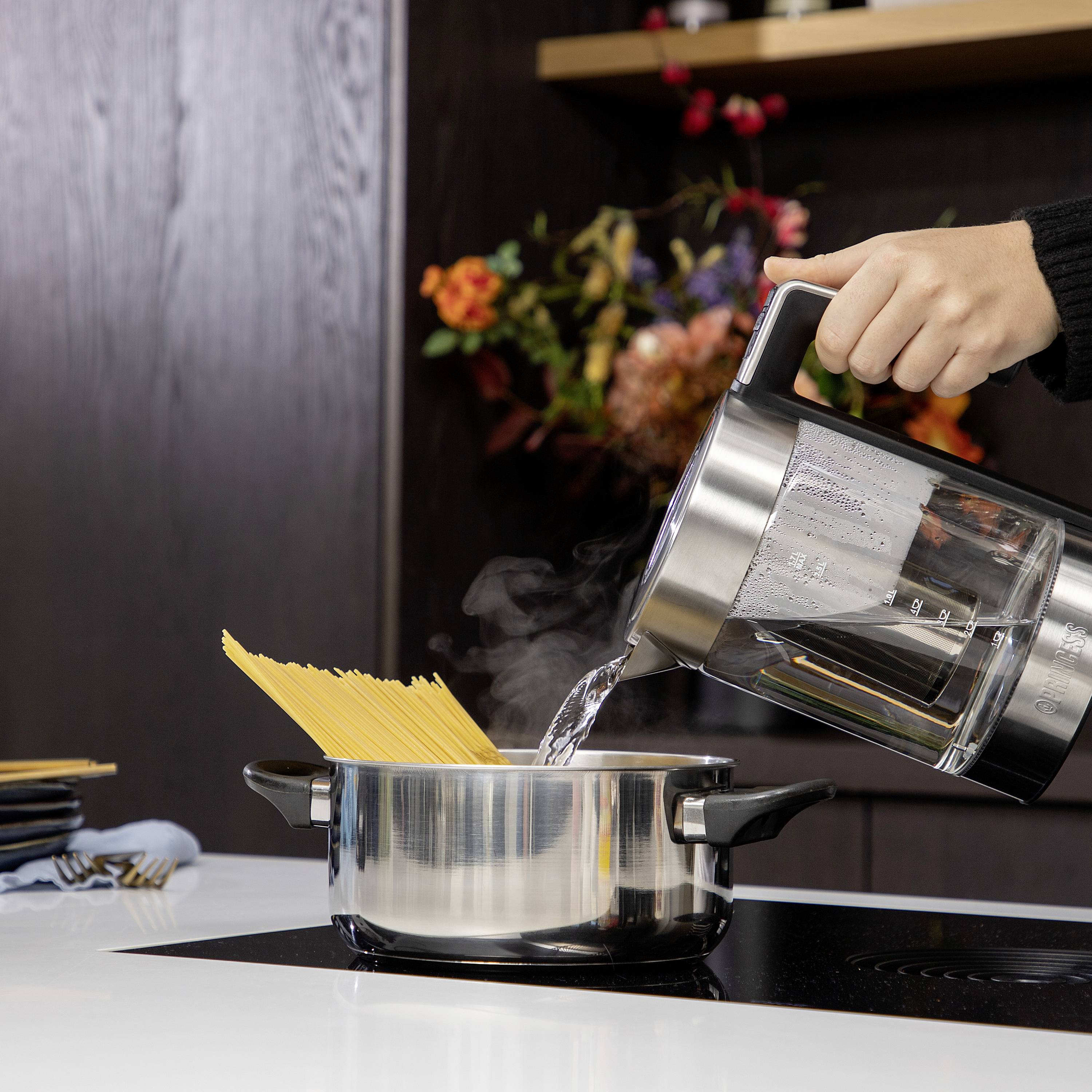 A hand pours hot water from a kettle into a saucepan of spaghetti. Flowers can be seen in the background.