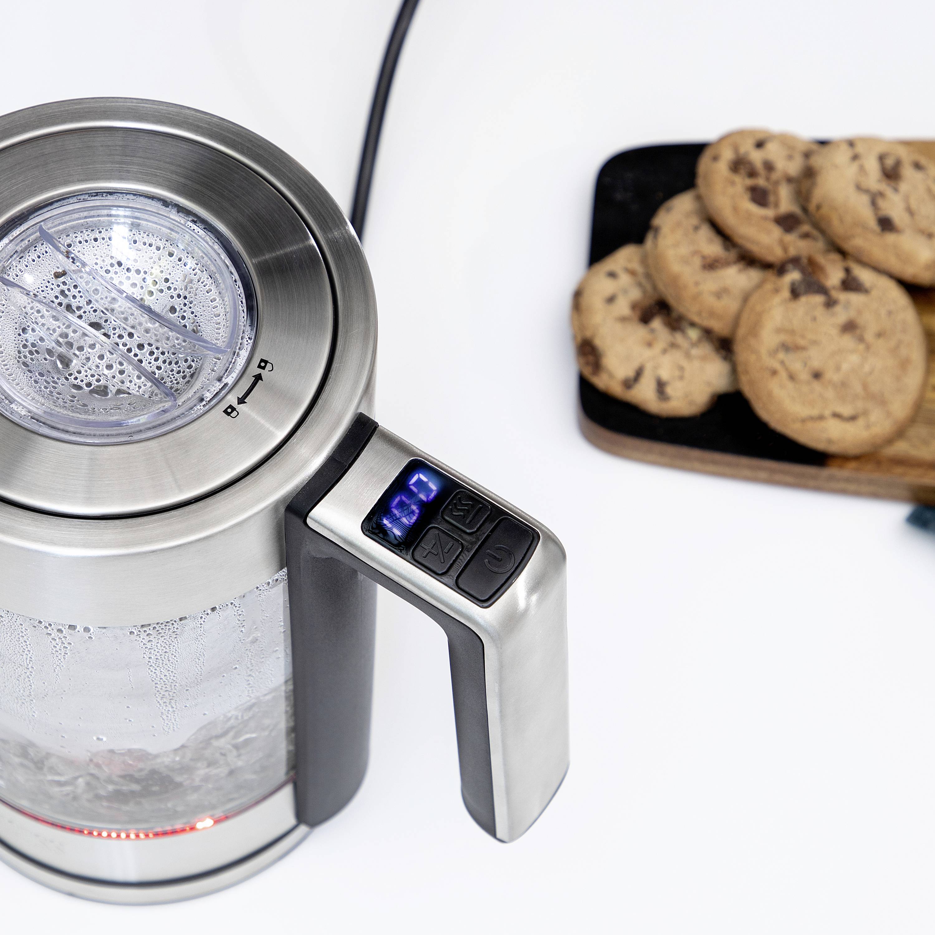 An electric kettle on a worktop is heating water. Beside it is a tray with chocolate biscuits.