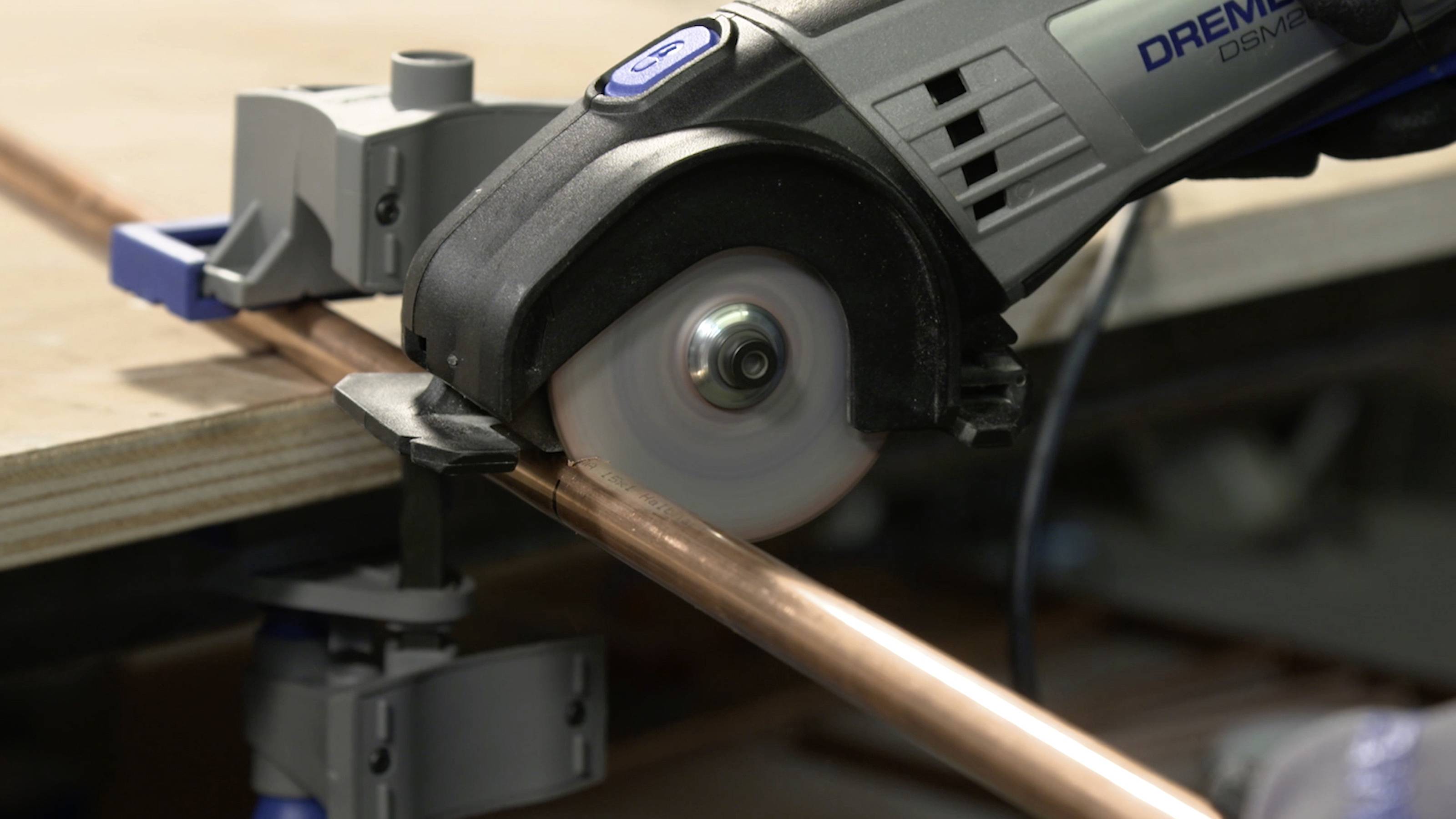 An electric saw cuts through a copper pipe that is secured to a table.