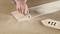 A hand is using an electric tool to saw wood. Sawdust surrounds the work area. A cut piece of wood lies beside it.