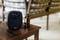 A speaker on a wooden table shows 'Stand by' on the display. Chairs and a brown bottle are blurred in the background.