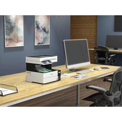 A printer sits on a wooden desk, surrounded by a computer, chairs and paper documents in a modern office.