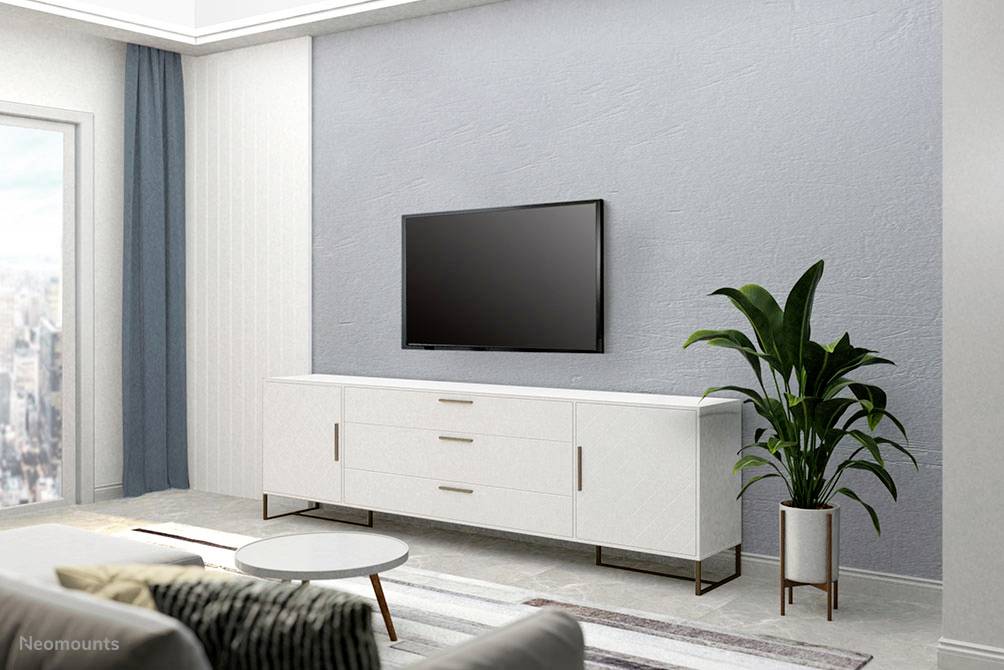 A modern living space with a television mounted on the wall above a white sideboard. A plant is positioned to the right beside it.