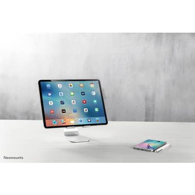 Tablet on a stand next to a smartphone on a table. Screen displays various app icons. Modern, minimalist look.