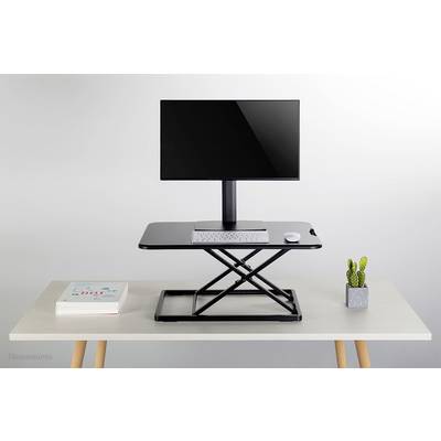 A height-adjustable desk riser with a monitor, keyboard, and mouse on top. Beside it, a stack of books and a small cactus.