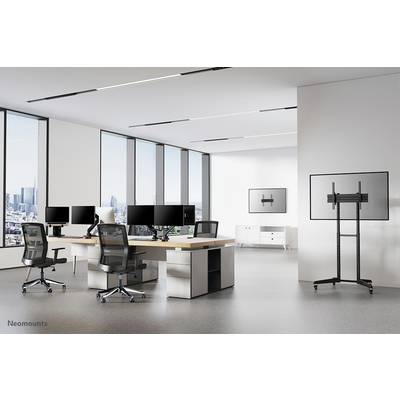Modern office environment with multiple desks, office and screen chairs, view of the city through large windows in the background.
