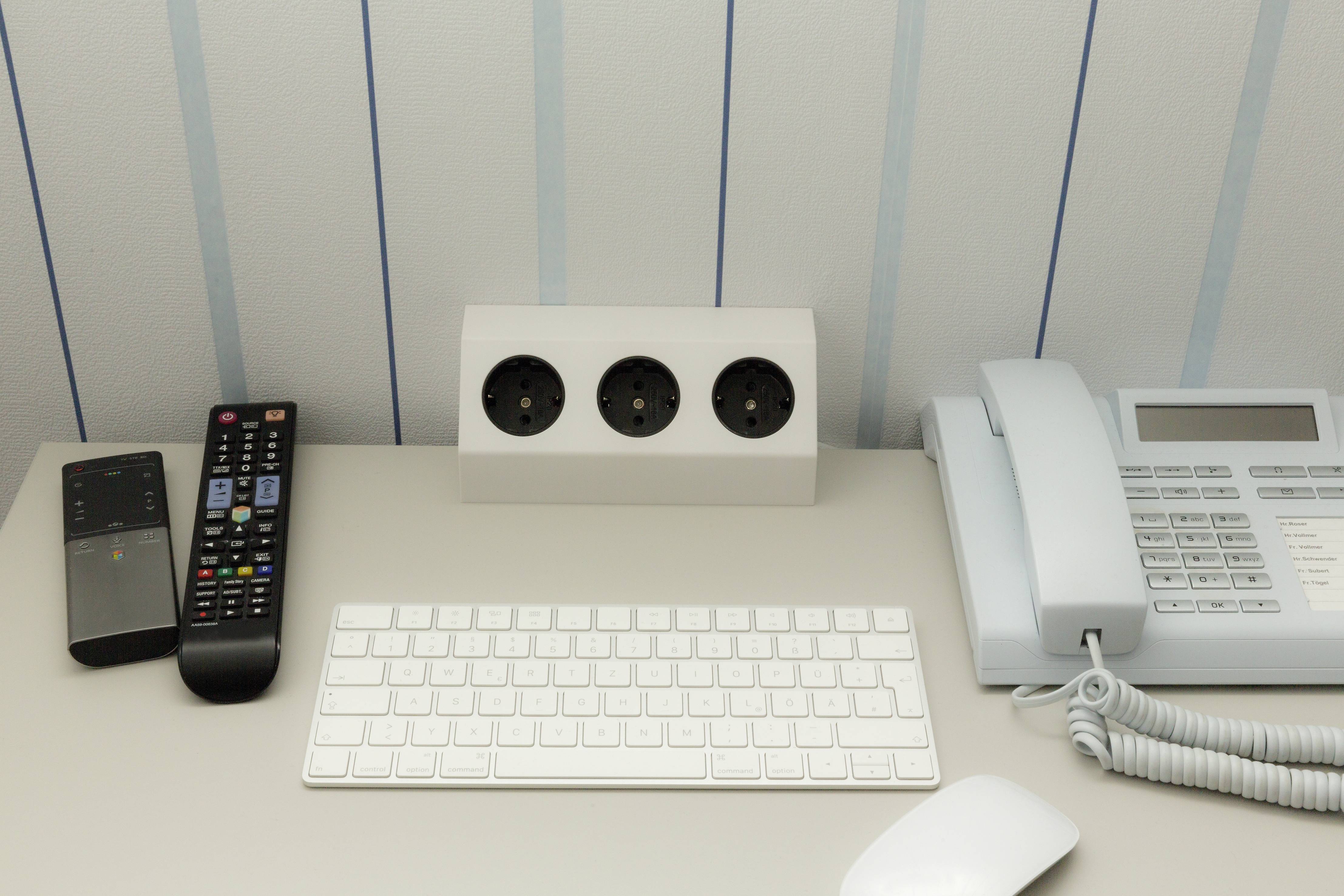Keyboard, two remote controls, telephone and power sockets on a table.