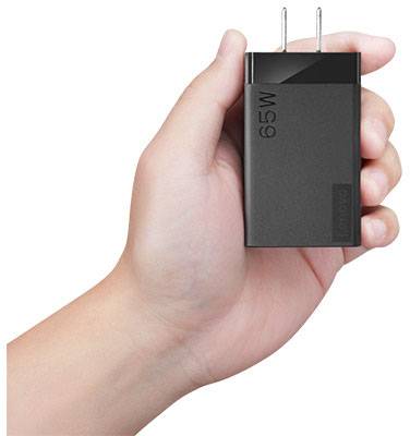 A hand holds a black charger with the inscription '65W', suitable for fast charging electronic devices.