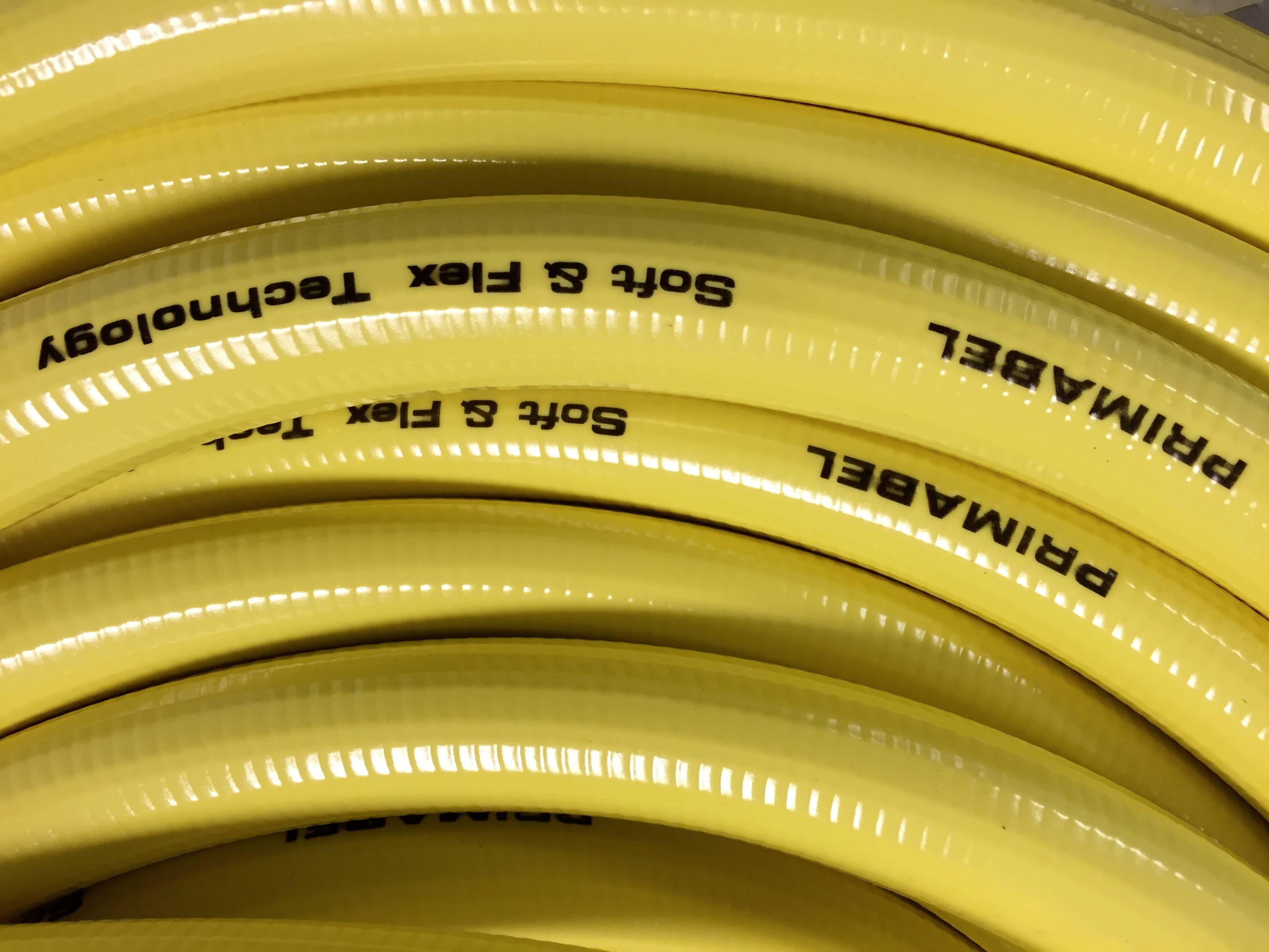 Yellow flexible hoses with the inscription 'Soft & Flex Technology', tightly coiled and stacked. They may potentially be used for transporting liquids.