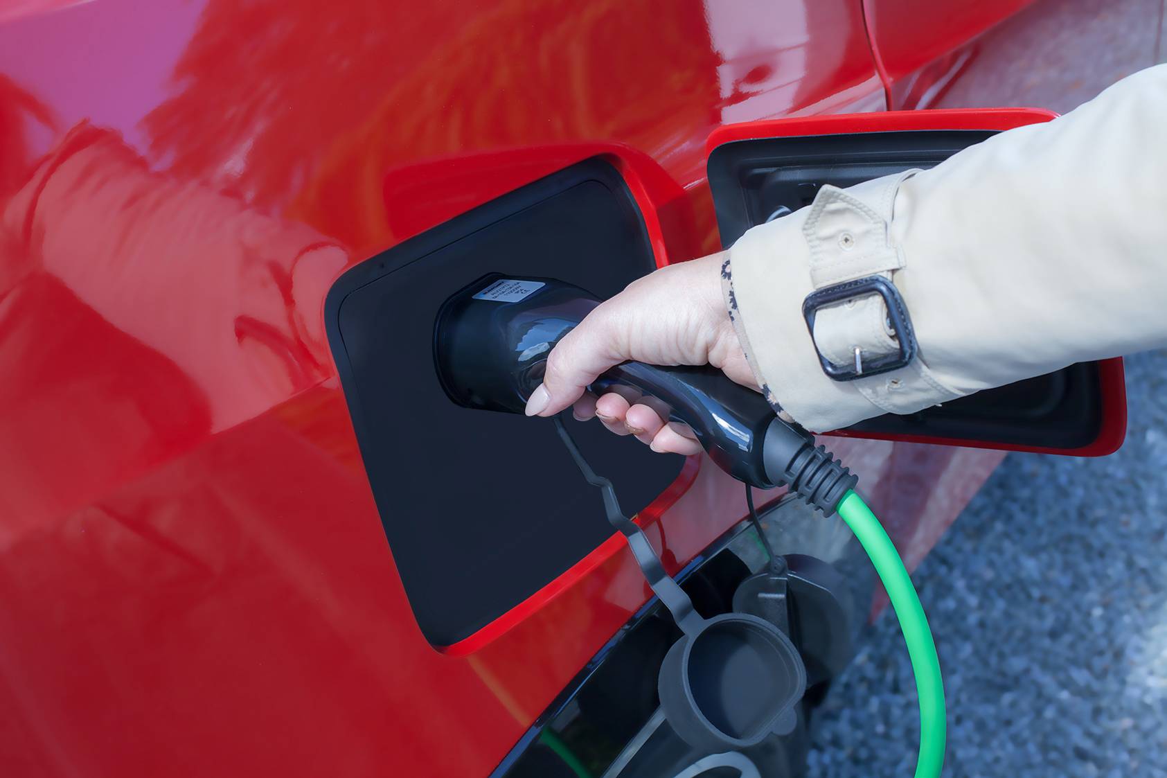 A person is holding a charging cable connected to a red electric car. It illustrates the charging of an electric vehicle.