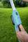 A person is holding a blue electric garden tool handle with a black switch against a green lawn background.