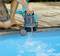 A person is using an electric pump to drain water from a swimming pool. The pump is black and blue with an orange detail.