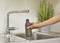 A hand is holding a water bottle under a running tap in a kitchen; a plant stands nearby.