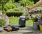 A person is pouring water into an irrigation pump on a wooden table in the garden, surrounded by flowering plants in pots.