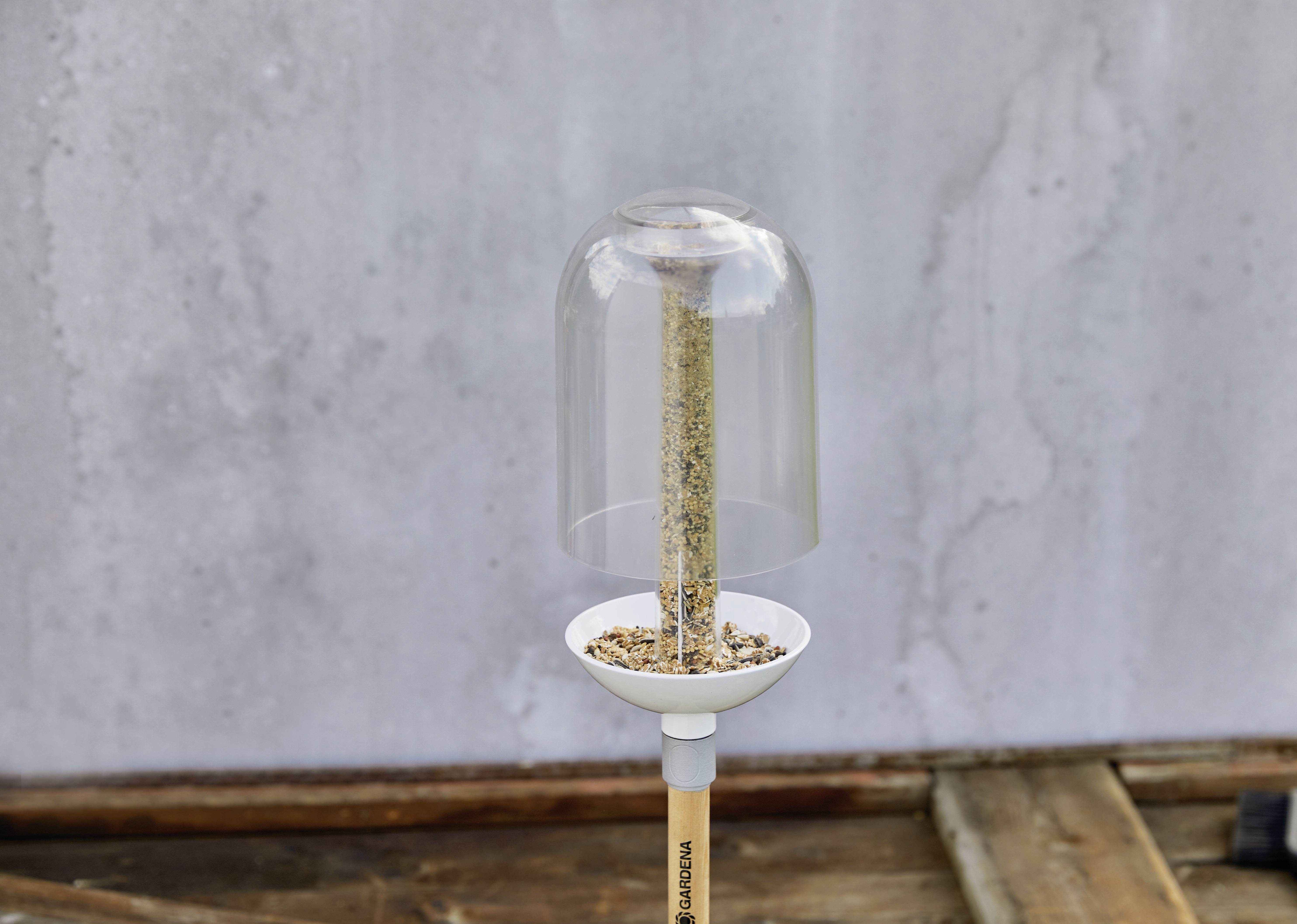 A slender rod device stands on a wooden table. A glass cylinder is inverted over its upper part.