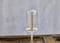 A slender rod device stands on a wooden table. A glass cylinder is inverted over its upper part.