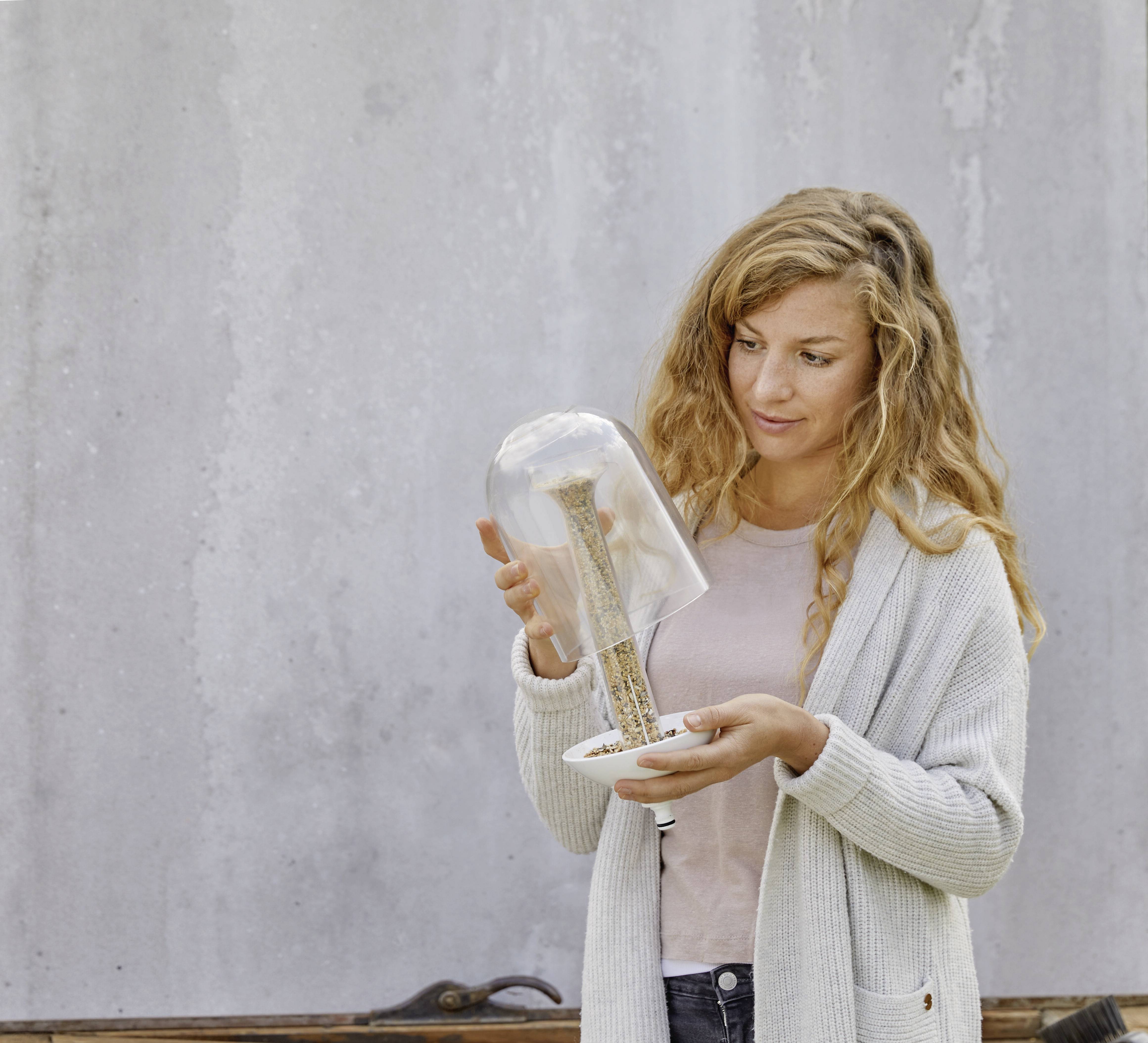 A woman is holding a glass sculpture resembling an hourglass. She is standing in front of a light grey wall.