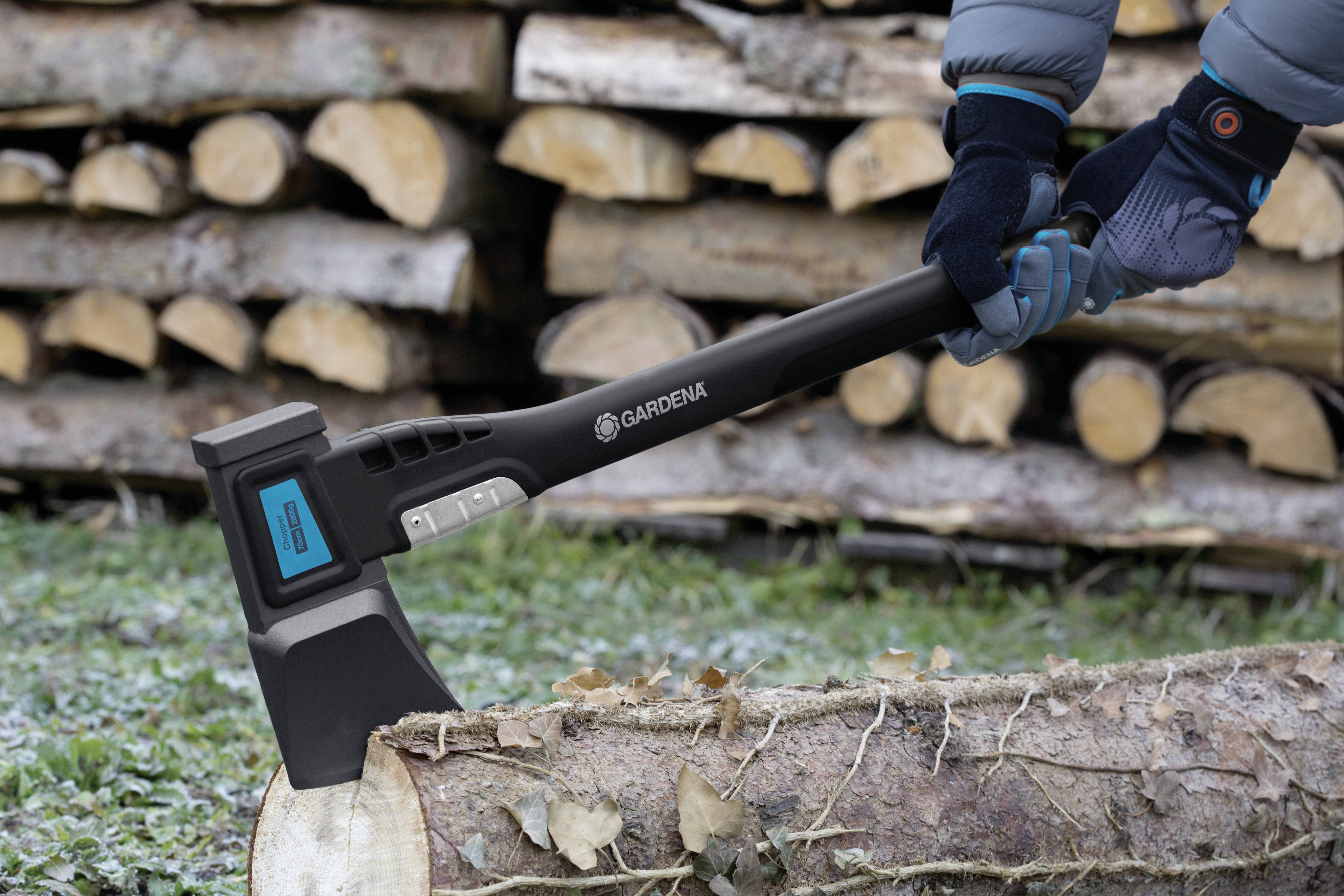 A person is splitting a log with an axe. Stacked logs can be seen in the background.