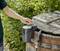 A person is operating an electric pump on a wooden barrel outdoors, surrounded by green plants.