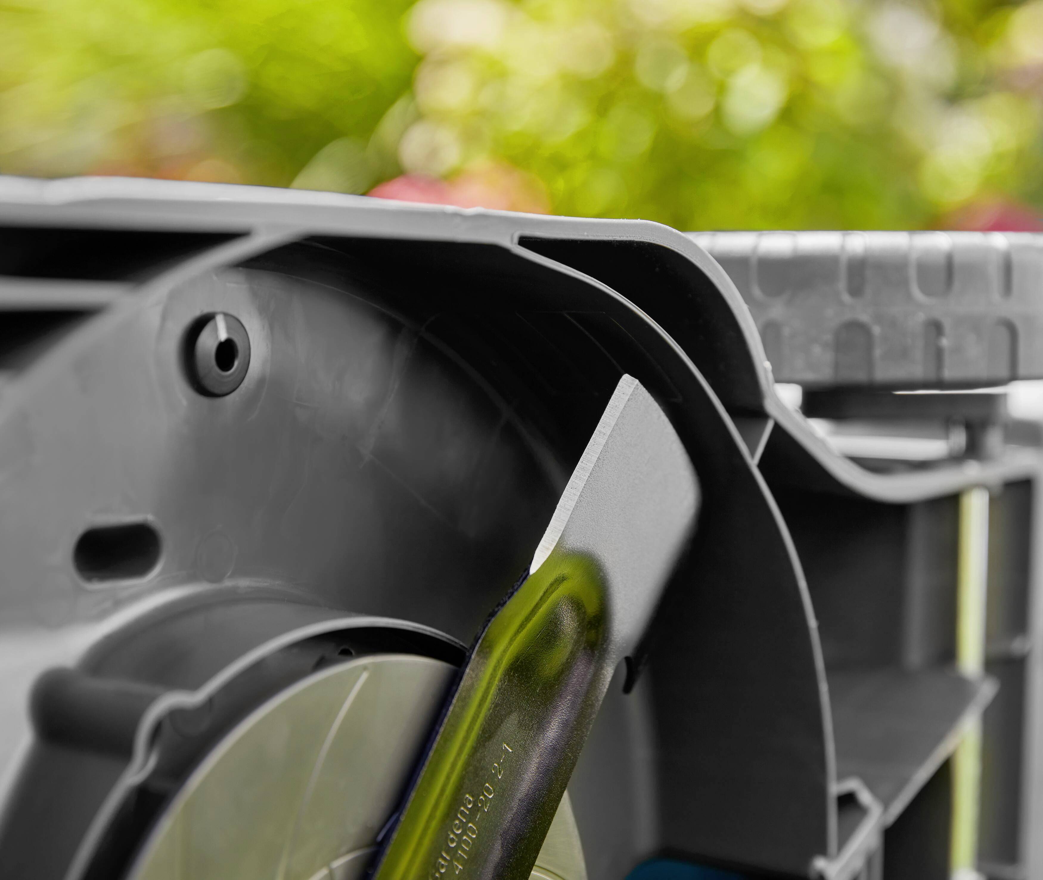Close-up of a garden tool with a rotating, metallic component against a green, blurred garden background.