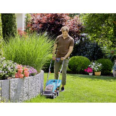A man is mowing the lawn with an electric lawnmower in a well-maintained garden, surrounded by colourful flowers and shrubs.