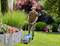 A man is mowing the lawn with an electric lawnmower in a well-maintained garden, surrounded by colourful flowers and shrubs.