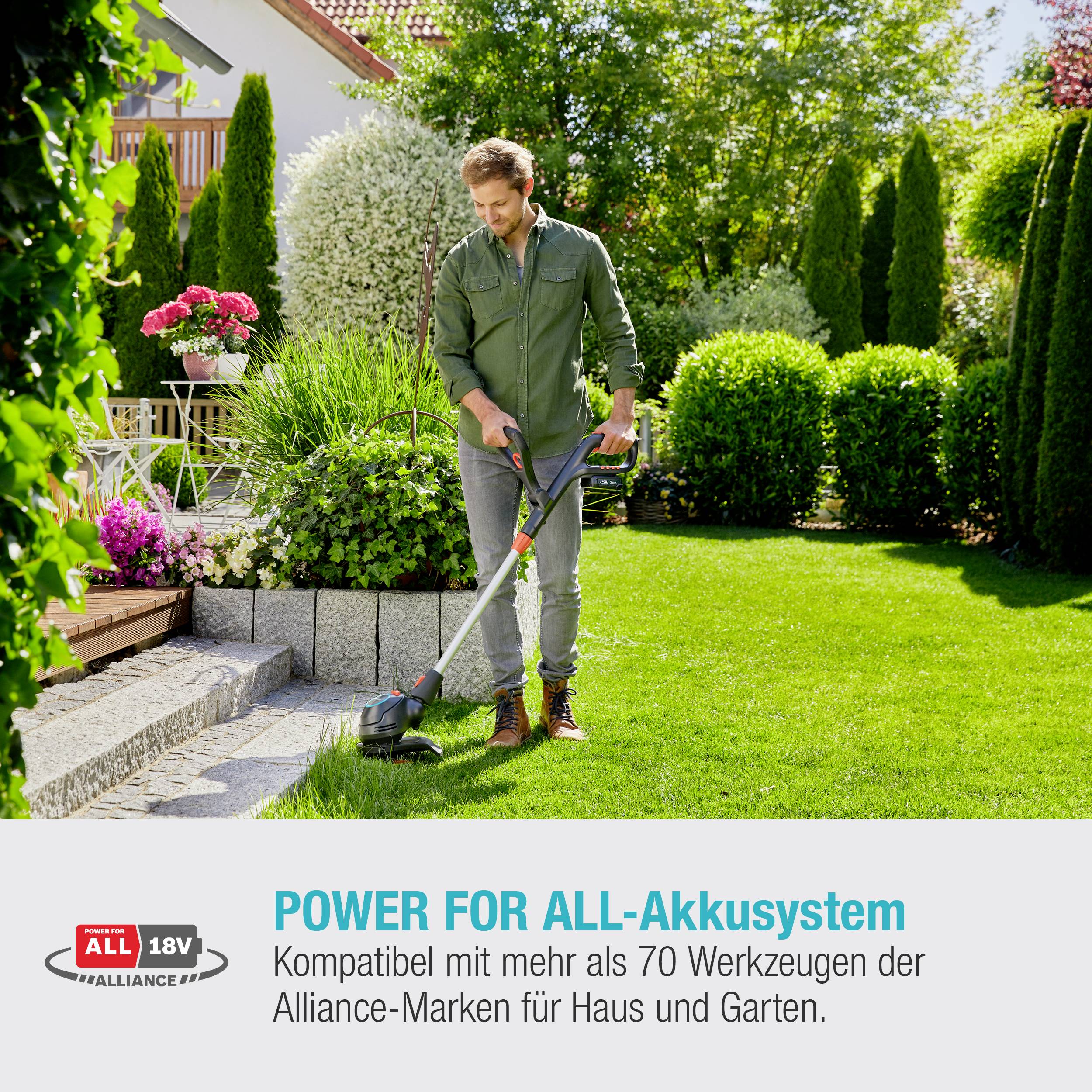 A person carefully trims the lawn next to a residential hedge using a battery-powered strimmer, surrounded by flowering plants.