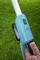 A person is holding a blue garden tool with a long handle. Green grass is visible in the background.