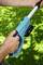 A person is holding a blue garden tool with a battery on green grass. Their hands are positioned on the handle.