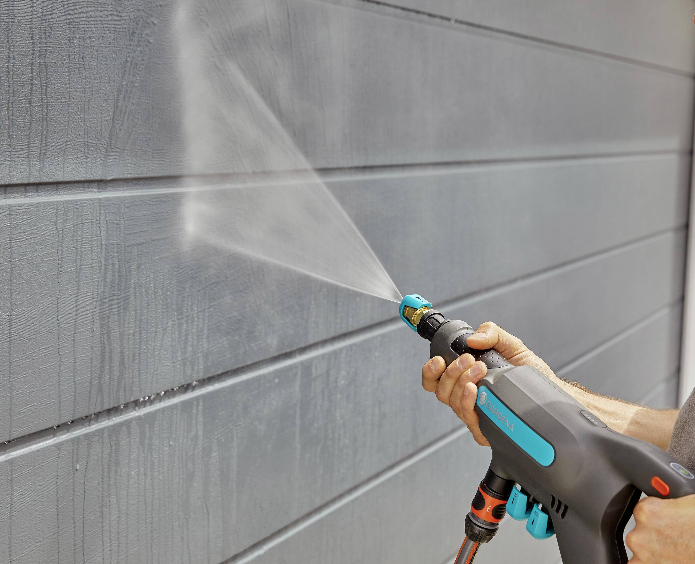 A person is cleaning a grey wall with a pressure washer.