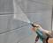 A person is cleaning a grey wall with a pressure washer.