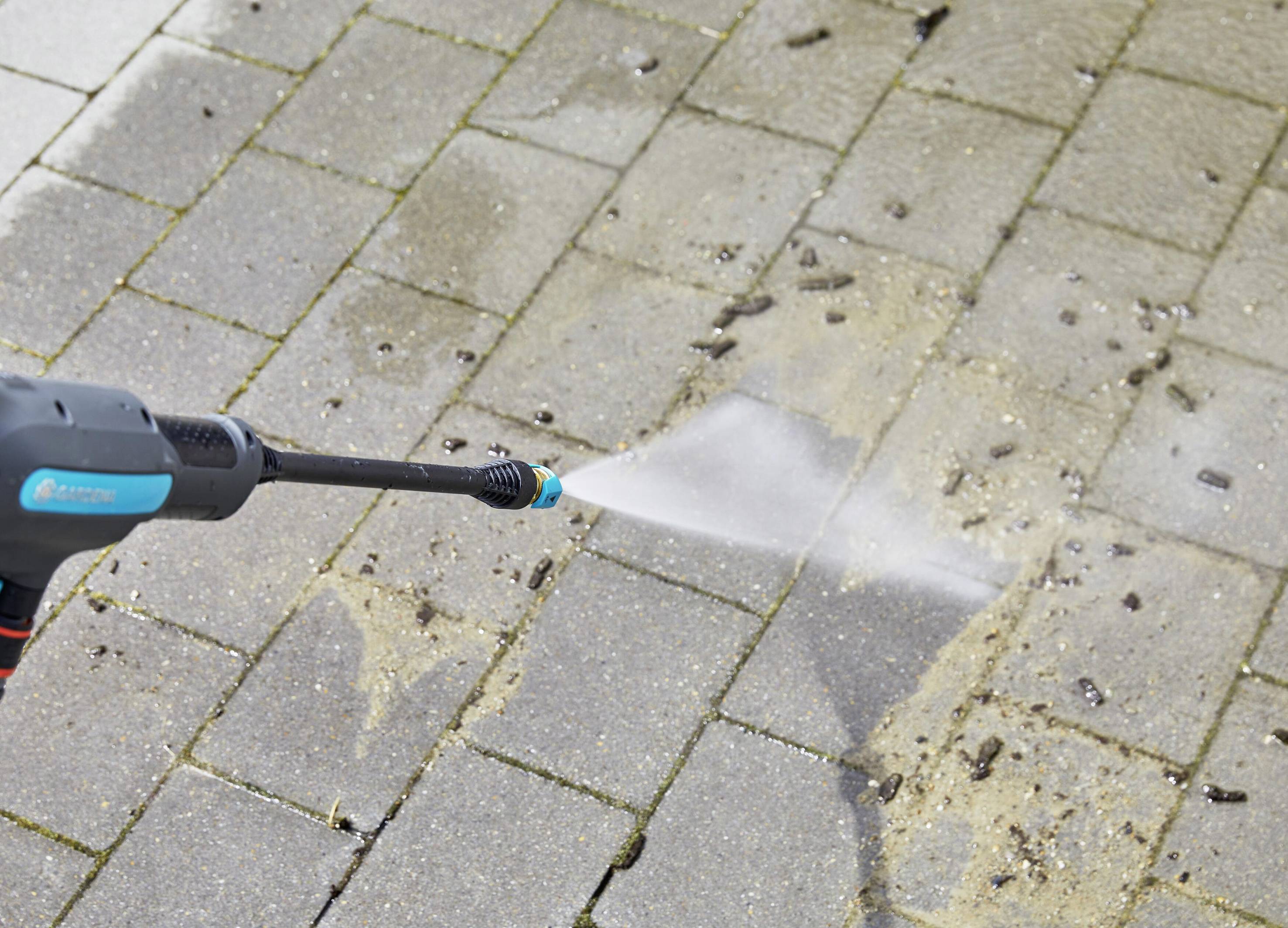 Close-up of a pressure washer cleaning paving stones. Water jet removes dirt and sand from the surface of the stones.