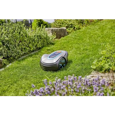 A robotic lawnmower moves across a green lawn between various plants and flowers in a garden.