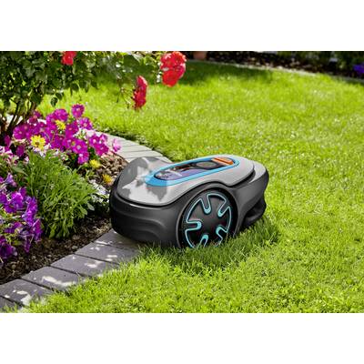 A robotic lawnmower is cutting grass beside a flower bed with colourful flowers on a green lawn.