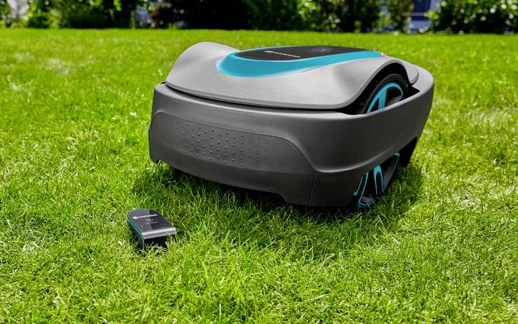 A robotic lawn mower on green grass with its remote control beside it, ready for automated lawn maintenance.