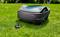 A robotic lawn mower on green grass with its remote control beside it, ready for automated lawn maintenance.