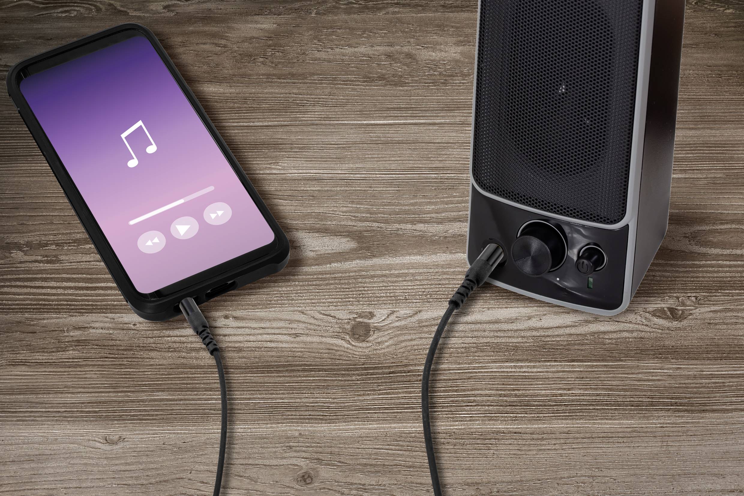 A smartphone connected to a speaker via an audio cable displays a music player on the screen.