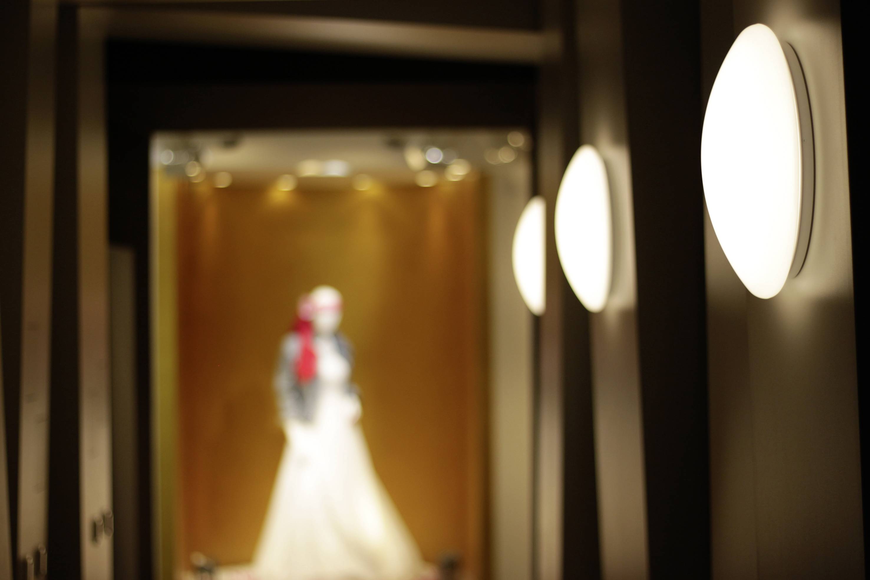 A mannequin illuminated in a well-lit corridor, wearing an elegant dress and a red hat.