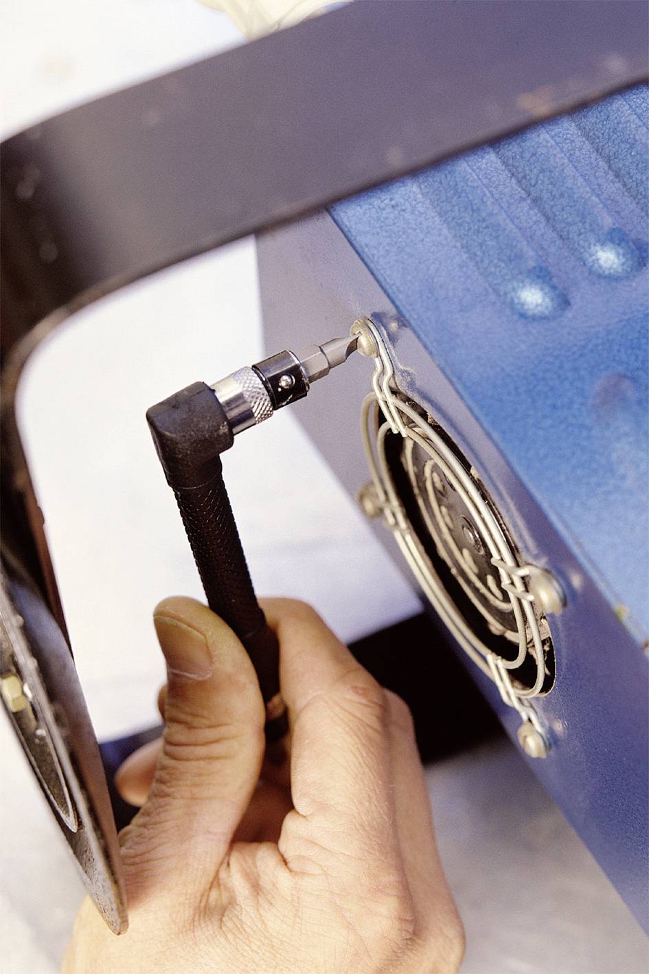 'Hand holding a screwdriver, fastening a fan to a blue casing.'