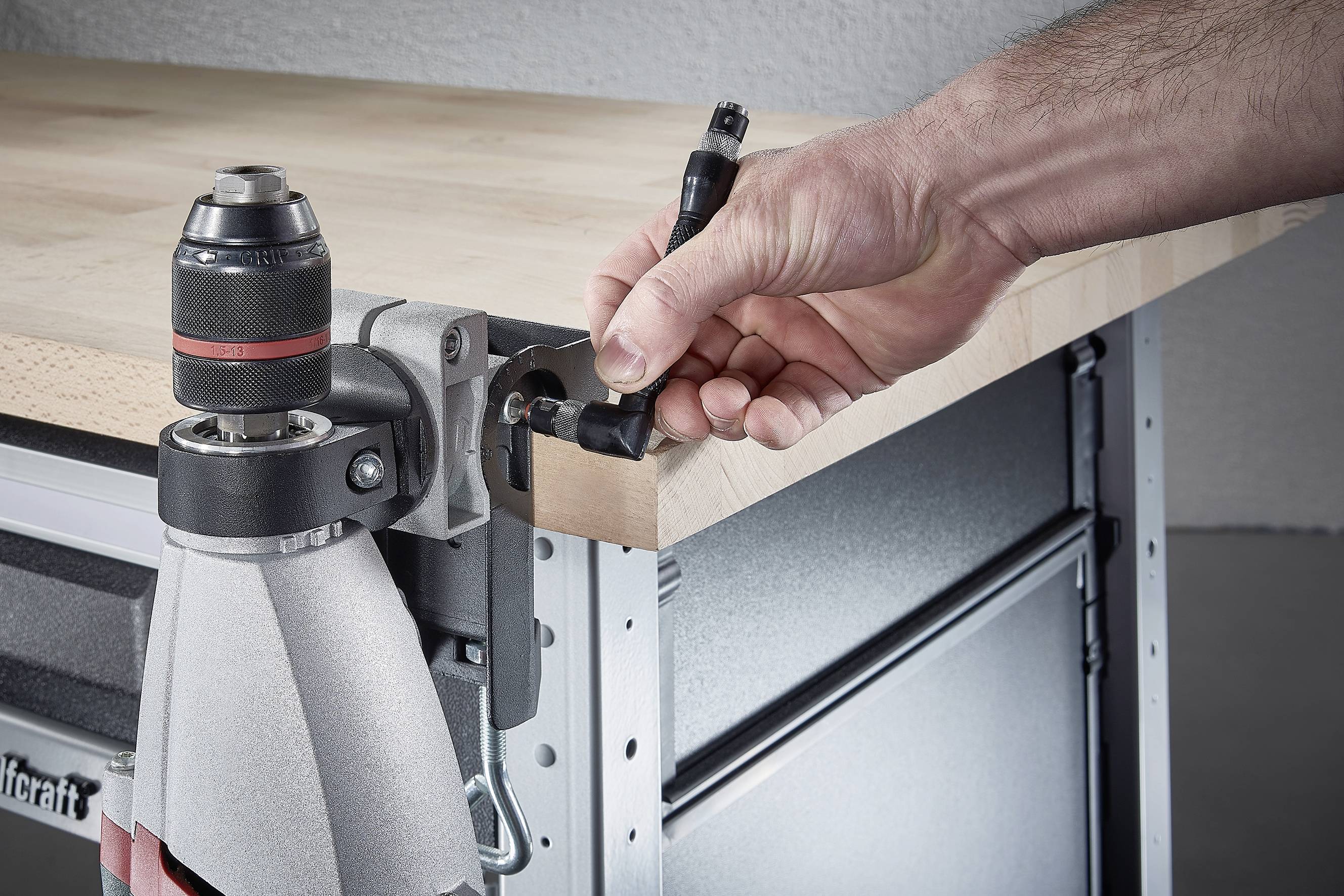 A hand is securing a wooden element to a metal frame on a workbench using a tool.